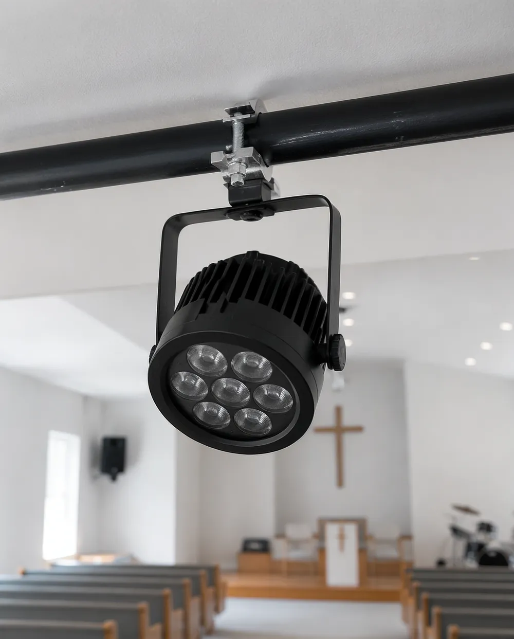 Compact LED par fixture mounted on pipe clamp in a low-ceiling church install