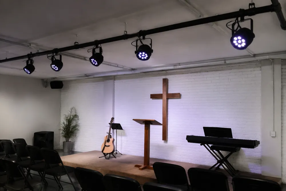 Simple church stage lighting — compact LED par fixtures mounted on low-ceiling pipe in a small worship venue