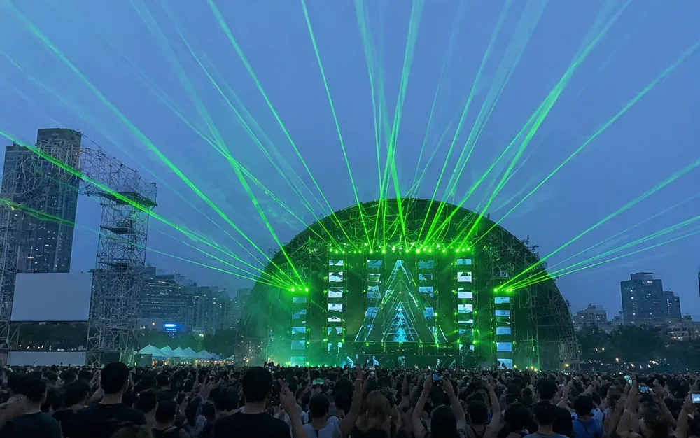 Green laser beams at outdoor festival creating long-throw aerial effects through haze