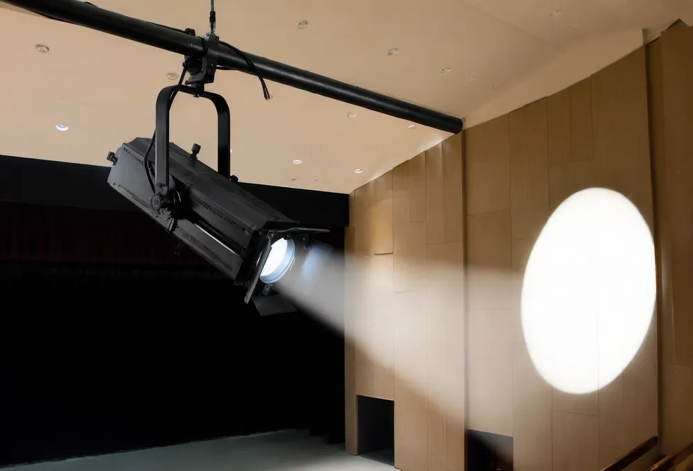 LED theatre profile spotlight with framing shutters mounted on lighting bar, illuminating stage with hard-edge beam