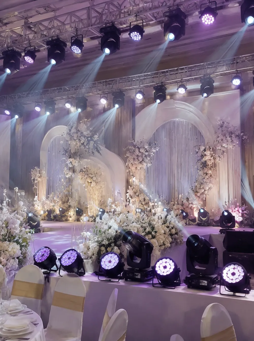 Wedding stage lighting fixtures in a decorated venue with warm LED wash and moving head beams