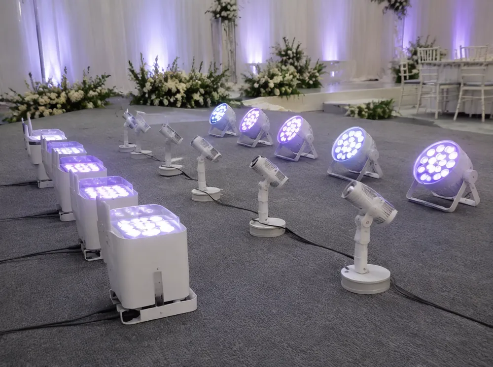 Wedding stage lighting fixtures — LED wash uplights, wireless PAR cans, and pin spots arranged for ceremony deployment